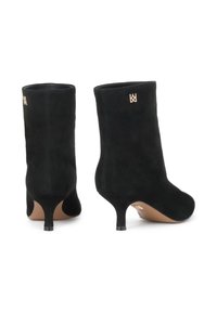 Botas de tobillo de ante negro con un diseño ajustado, que presentan un tacón delgado y un acento de logo dorado en el lado exterior. Textura suave, con detalles mínimos.