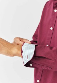 Bordeaux knoopshirt met een wit en lichtblauw gestreepte manchet. Heeft een zachte textuur en een klassiek kraagontwerp.