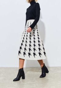 Acream skirt featuring a black houndstooth pattern, knee-length, paired with a black long-sleeve turtleneck and ankle boots.