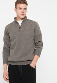 Γκρι πλεκτό πουλόβερ με μισό φερμουάρ στον λαιμό, ραμμένα μανίκια και ζώνη. Μαλακή υφή, χαλαρή εφαρμογή και λεπτές λεπτομέρειες στον λαιμό.