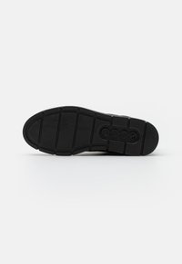 Suela de zapato de goma negra con un diseño de patrón, que presenta secciones distintas y logotipos grabados en la superficie. Diseño plano y texturizado.