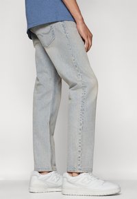 Lys blå denimjeans med rett snitt, sammen med hvite sneakers. Jeansene har en lett falmet tekstur og klassisk fem-lomme-design.
