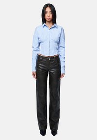 Blau-weiß gestreiftes, tailliertes Baumwollhemd, kombiniert mit hochgeschnittenen schwarzen Lederhosen; scharfer Kragen, Knopfdetails und weit geschnittenes Design.