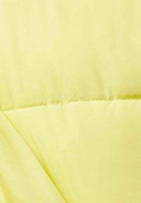Giacca imbottita in nylon giallo brillante con una texture liscia. Presenta cuciture visibili e una leggera lucentezza, creando un aspetto leggero.