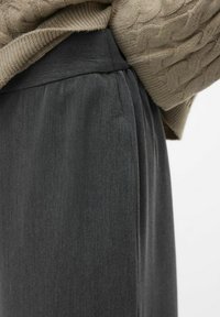 Szare plisowane spodnie o miękkiej teksturze i elastycznym pasie, częściowo przykryte jasnobeżowym swetrem z dzianiny.