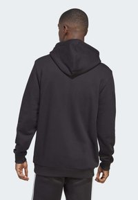 Felpa nera con cappuccio realizzata in tessuto testurizzato, caratterizzata da un ampio cappuccio e polsini a coste. Il retro presenta un design senza cuciture con un taglio dritto.