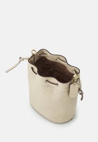 Borsa a secchiello in pelle beige con motivo a rilievo, parte superiore arrotondata, chiusura con coulisse e dettagli in metallo dorato. L'interno è foderato in suede e presenta tasche.