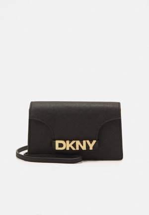 Pochette noire texturée DKNY avec logo doré sur le devant et une fine sangle de poignet attachée sur fond blanc.