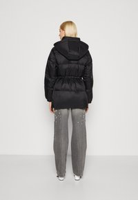 Doudoune noire avec capuche, ceinture élastique et design matelassé horizontal. Assortie à un pantalon large gris avec des accents éclaboussés.