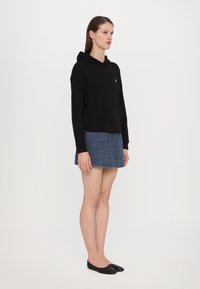 Svart kort hoodie med kengurulomme, kombinert med et denimminiskjørt med geometrisk mønster. Båret med svarte flate sko.