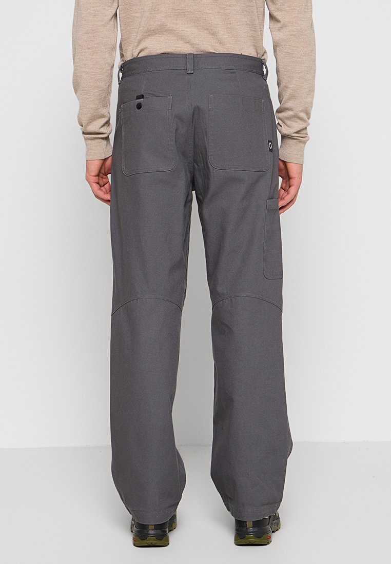 Pantalones cargo grises con múltiples bolsillos, rodillas reforzadas y corte recto, combinados con calzado negro sobre un fondo sencillo.