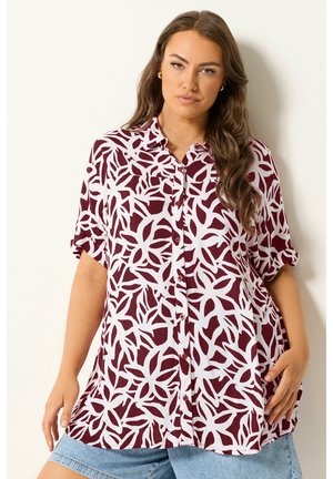 Kvinde iført bordeauxrød og hvid bladmønstret skjorte med korte ærmer, kombineret med lyseblå denimshorts.
