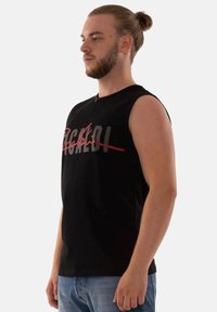 Schwarzes ärmelloses T-Shirt aus weichem Material, mit auffälligem grafischen Text in Rot und Grau. Figurumspielendes Design mit rundem Ausschnitt.
