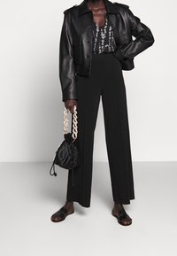 Giacca cropped in pelle nera sopra una top con motivo, abbinata a pantaloni larghi neri, sandali neri e una borsa arricciata con tracolla a catena.