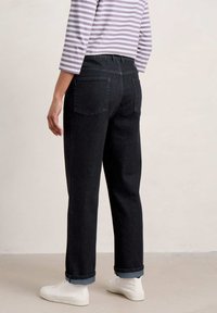 Tmavé džíny s volným střihem, s ohrnutými nohavicemi a dvěma zadními kapsami, doplněné pruhovaným tričkem s třičtvrtinovým rukávem a bílými teniskami.