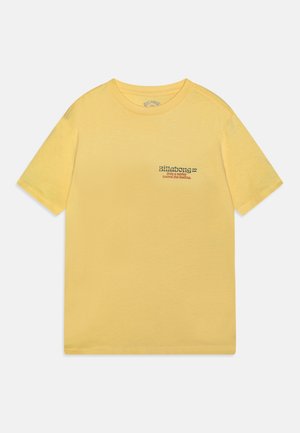T-shirt jaune à manches courtes avec le logo Billabong et le texte « Only a surfer knows the feeling » sur le côté gauche de la poitrine.