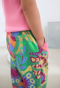 Bunte Cordhosen mit einem Blumenmuster in Grün, Pink, Orange und Blau, mit einer Seitentasche und texturiertem Stoff. Pinkes geripptes Oberteil.