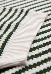 Textil de rayas verdes y blancas con un borde ribeteado blanco, tejido texturizado con patrón en zigzag, con un aspecto suave y de punto.