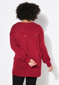 Roter gestrickter Pullover mit offenen Ausschnitten am Rücken, gerippten Bündchen und Saum. Lange Ärmel, lockere Passform und strukturiertes Material.