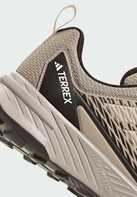 Gros plan sur le talon de la chaussure de trail Terrex beige et marron avec une semelle texturée et une tige en mesh.