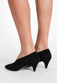 Escarpins en daim noir avec un bout pointu et un talon kitten de 2 pouces. Présentent un accent rouge subtil à l'arrière et une surface lisse et texturée.