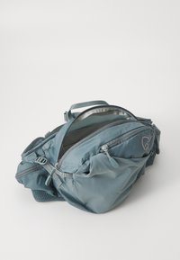 Zaino in nylon blu con numerosi scomparti con zip, tessuto testurizzato e un pannello in rete. Presenta un piccolo logo sul lato.