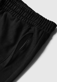 Zwarte sweatpants met een geribde tailleband en zijzakken met rits, gemaakt van zachte, gestructureerde stof, ontworpen voor comfort en veelzijdigheid.