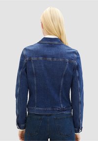 Tmavě modrá džínová bunda s přiléhavým střihem, švem na zadním dílu a knoflíky na manžetách. Texturovaná látka s klasickým střihem.