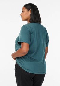 Teal t-shirt med kort ärm, rundad nederkant och avslappnad passform, tillverkad av mjukt material. Synliga sömmar på ärmarna.