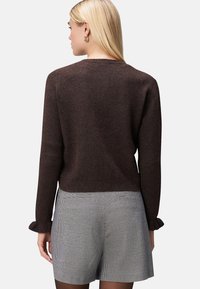 Maglione marrone lavorato a maglia con maniche lunghe, scollatura rotonda e una texture sottile. Abbinato a pantaloni corti a quadri con orlo arricciato.