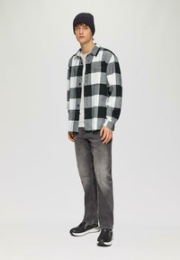 Zwart-wit geruit flanellen overhemd met knoopsluiting, gedragen over een grijze t-shirt, gecombineerd met grijze jeans en zwarte sneakers.