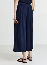 Pantalon large marine en tissu doux avec une taille élastique et une coupe fluide. Associé à des sandales plates noires pour un look décontracté.
