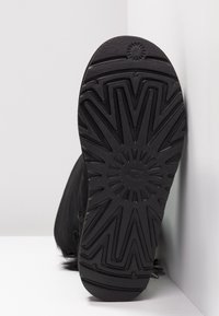 Semelle d'une botte d'hiver noire avec un motif de bande de roulement en zigzag profond et un logo circulaire au centre, sur fond blanc.