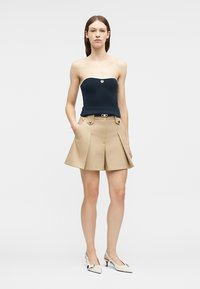 Fiatal nő vállpánt nélküli tengerészkék felsőben fehér szegéllyel, bézs magasderekú zsebes rövidnadrágban és fehér alacsony sarkú cipőben.