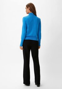 Blauer Pullover mit hohem Kragen, taillierter Passform und gerippten Bündchen, kombiniert mit schwarzen weit geschnittenen Hosen. Glatte Textur, einfache Nähte.