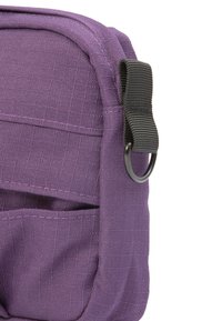 Lila Stofftasche mit strukturiertem Material, ausgestattet mit einem schwarzen Tragegurt und einem Metallring. Enthält Außentaschen für eine bessere Organisation.