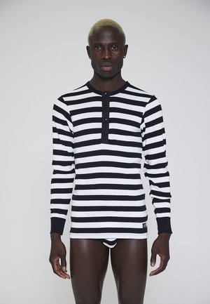 Sort og hvid stribet langærmet bluse med rund halsudskæring og tre-knaps placket. Stoffet virker blødt med ribbet detaljering på manchetterne.