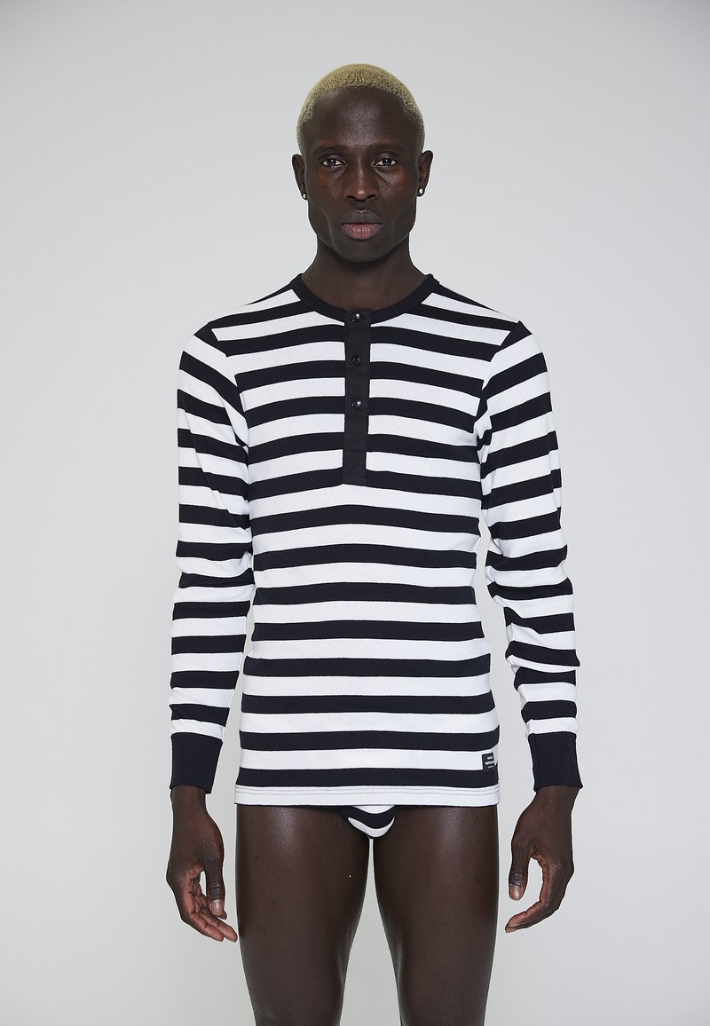 Sort og hvid stribet langærmet bluse med rund halsudskæring og tre-knaps placket. Stoffet virker blødt med ribbet detaljering på manchetterne.