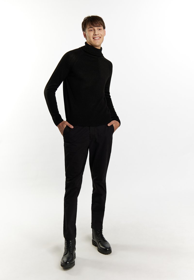 Schwarzer Rollkragenpullover mit Rippendesign, kombiniert mit schwarzen, taillierten Hosen und schwarzen Schnürstiefeln. Glatte Textur durchgehend.