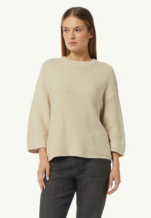 Beige gestrickter Pullover mit rundem Halsausschnitt und weiten, kurzen Ärmeln. Strukturierter Stoff mit lässiger Passform, kombiniert mit dunklen Jeans.
