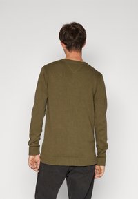 Oliivinvihreä ribbineulospusero, jossa on pitkät hihat, pyöreä pääntie ja teksturoidtu pinta. Suora helma ja istuvat hihansuut.