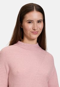 Hellrosa, geripptes Sweatshirt mit hohem Kragen und langen Ärmeln. Verfügt über diagonale Nahtdetails und eine weiche Textur.