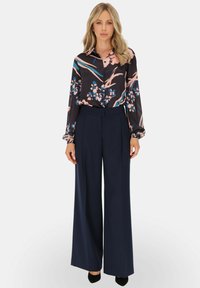 Czarna bluzka w kwiaty z długimi rękawami, w odcieniach różu i niebieskiego; zestawiona z wysokim stanem, szerokimi granatowymi spodniami.