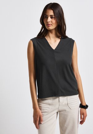 Haut sans manches noir avec un col en V et un drapé subtil ; fabriqué à partir d'un tissu lisse. Porté avec un pantalon ajusté de couleur claire.
