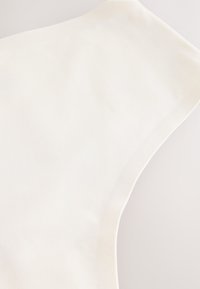 Gros plan de la partie supérieure d'un vêtement blanc sans manches avec une texture lisse et une couture propre le long de l'emmanchure.