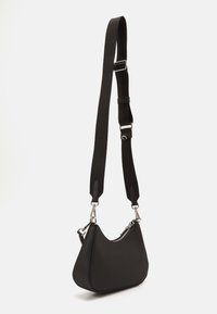 Sac à bandoulière noir à la forme arrondie, surface texturée, bandoulière en tissu réglable, et accastillage en métal ton argenté. Compartiment principal avec fermeture éclair.