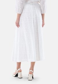 Weiße bestickte A-Linien-Rock mit floralen Mustern. Kombiniert mit cremefarbenen Blockabsatzsandalen. Glatte Textur und knöchellanges Design.