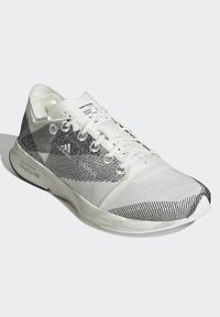 Zapatilla deportiva blanca con parte superior texturizada en blanco y negro, diseño ligero, cierre con cordones y detalles de marca en el lateral y la lengüeta.