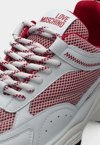 Λευκό και κόκκινο αθλητικό παπούτσι από δίχτυ με χοντρά λευκά κορδόνια, διακοσμητική ραφή ζιγκ-ζαγκ και το κείμενο "LOVE MOSCHINO" στη γλώσσα.