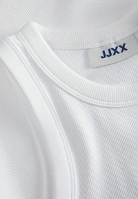 Hvid ribbet tanktop med rund halsudskæring. Har et mærke med navnet "JJXX" i blåt. Glat tekstur med fine vandrette linjer.